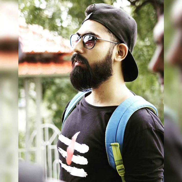 Man with beard wearing sunglasses, black cap, and WYO black t-shirt with graphic design, standing outdoors.