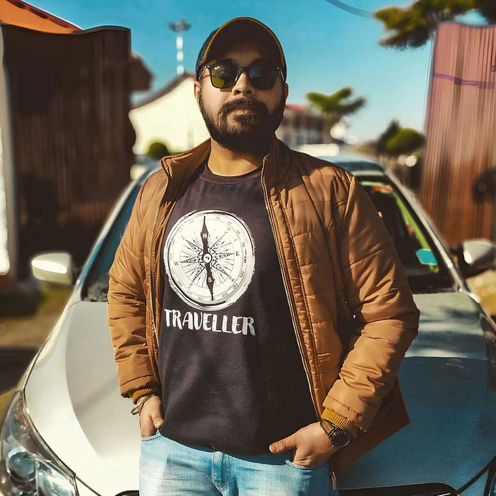 Man wearing a WYO 'Traveller' t-shirt and brown jacket standing next to a car.