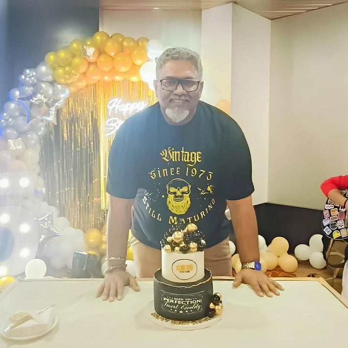 Man standing behind a cake with balloons and decorations in the background wearing WYO custom t-shirt