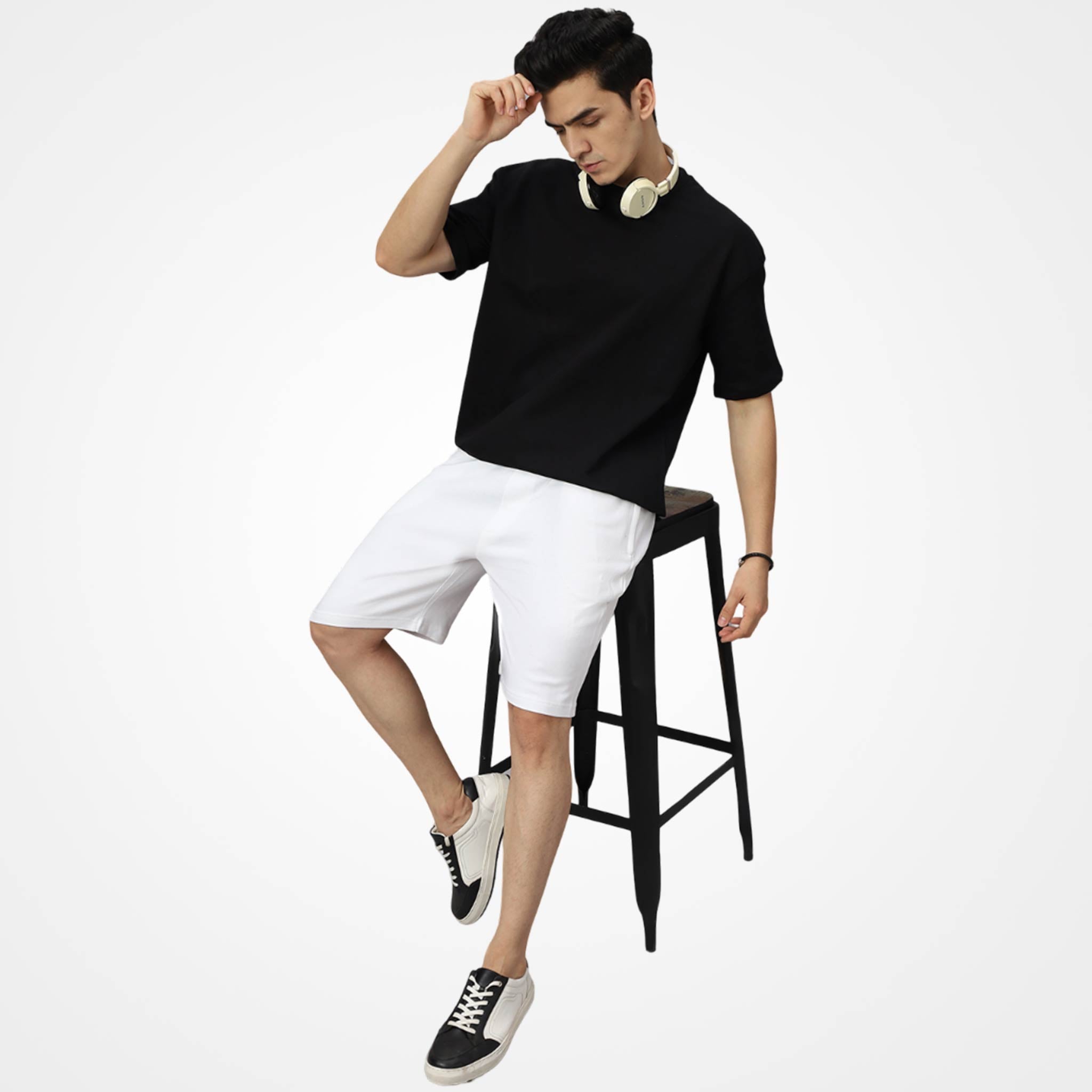 Man wearing a WYO black t-shirt and white shorts sitting on a black stool against a white background