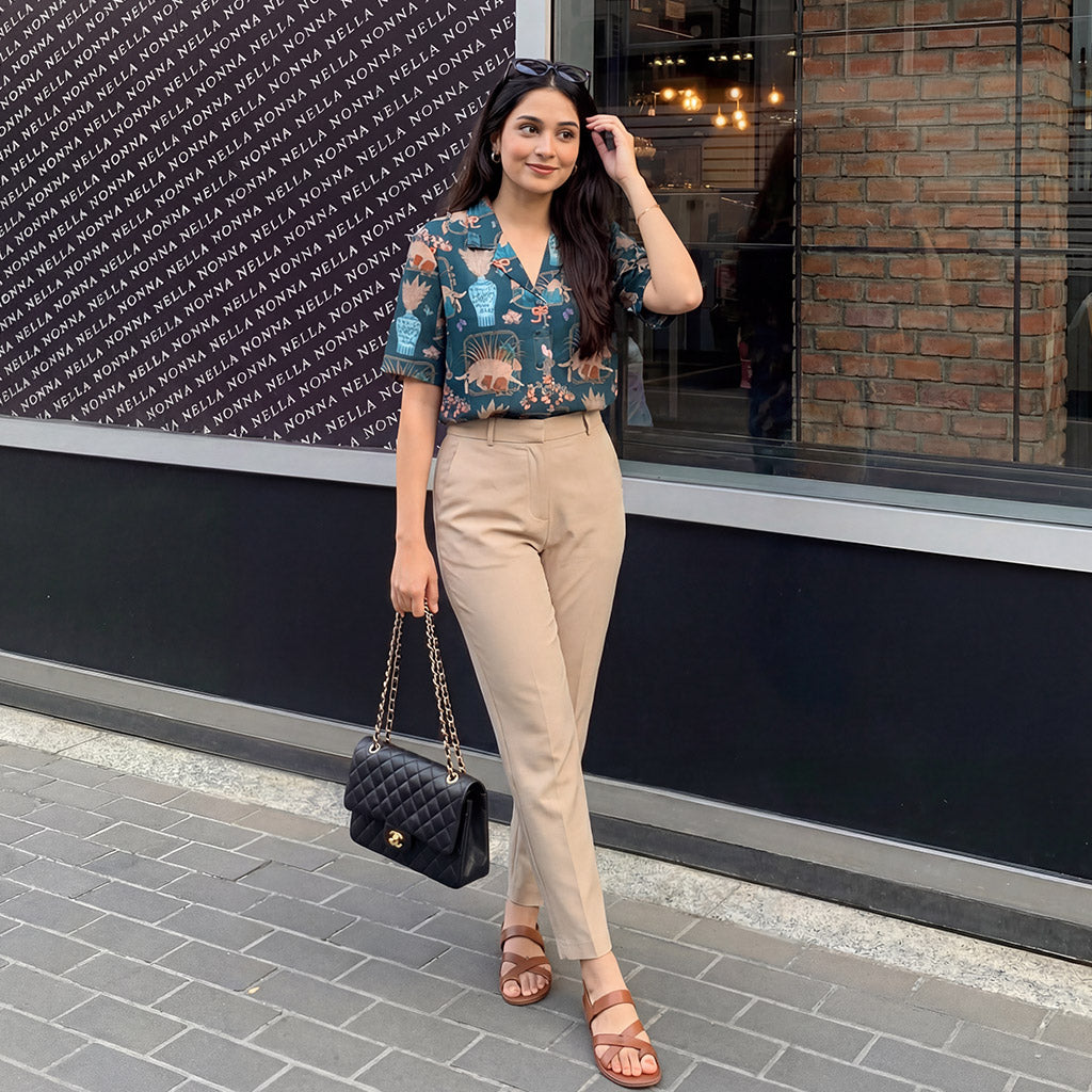 Woman in a WYO floral shirt and beige pants standing in front of a store with a black wall.