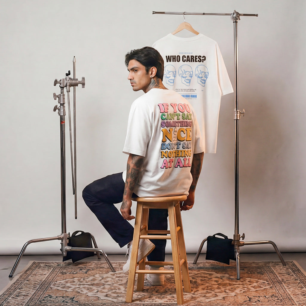 Man sitting on a stool wearing a WYO white t-shirt with colorful text, with another t-shirt on a rack in the background.