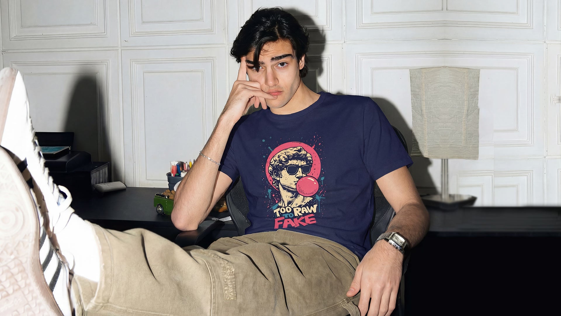 Man wearing a graphic t-shirt by WYO and sitting in a room with a lamp and desk.