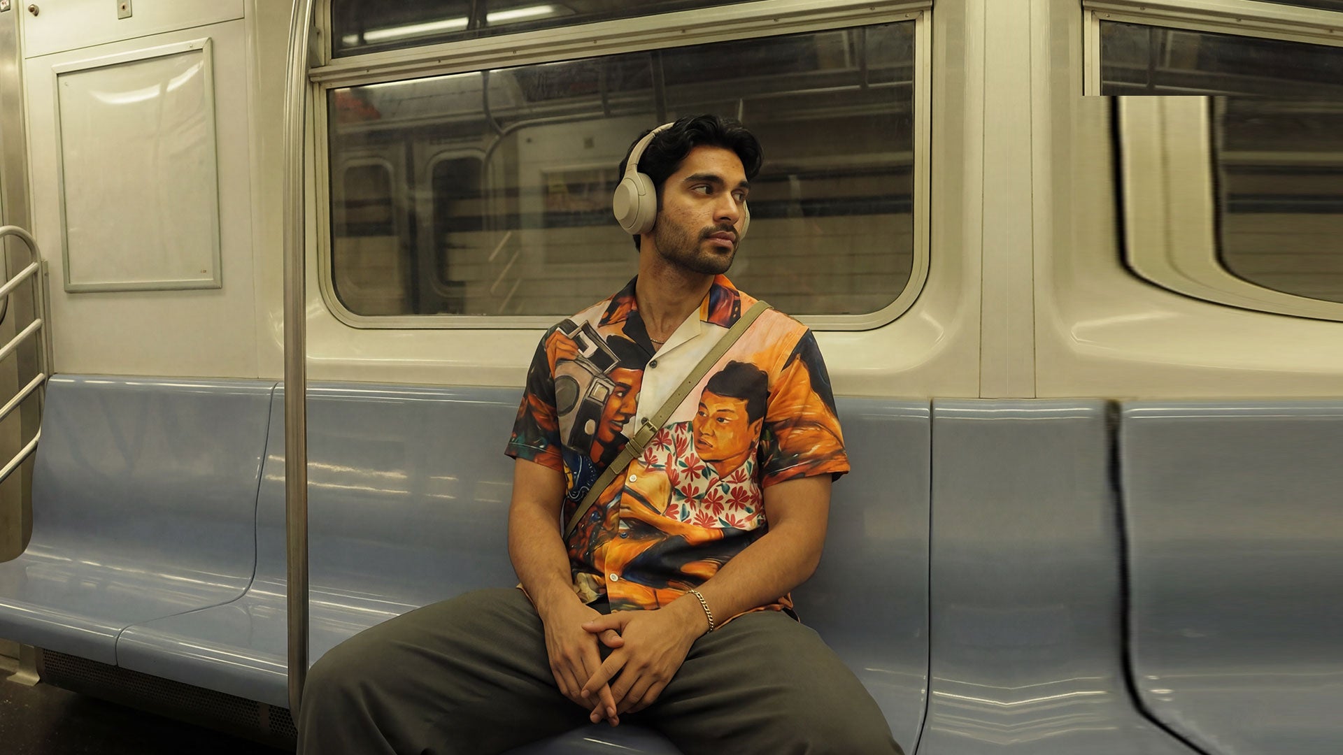 Man sitting on a subway train wearing headphones and a colorful shirt by WYO.