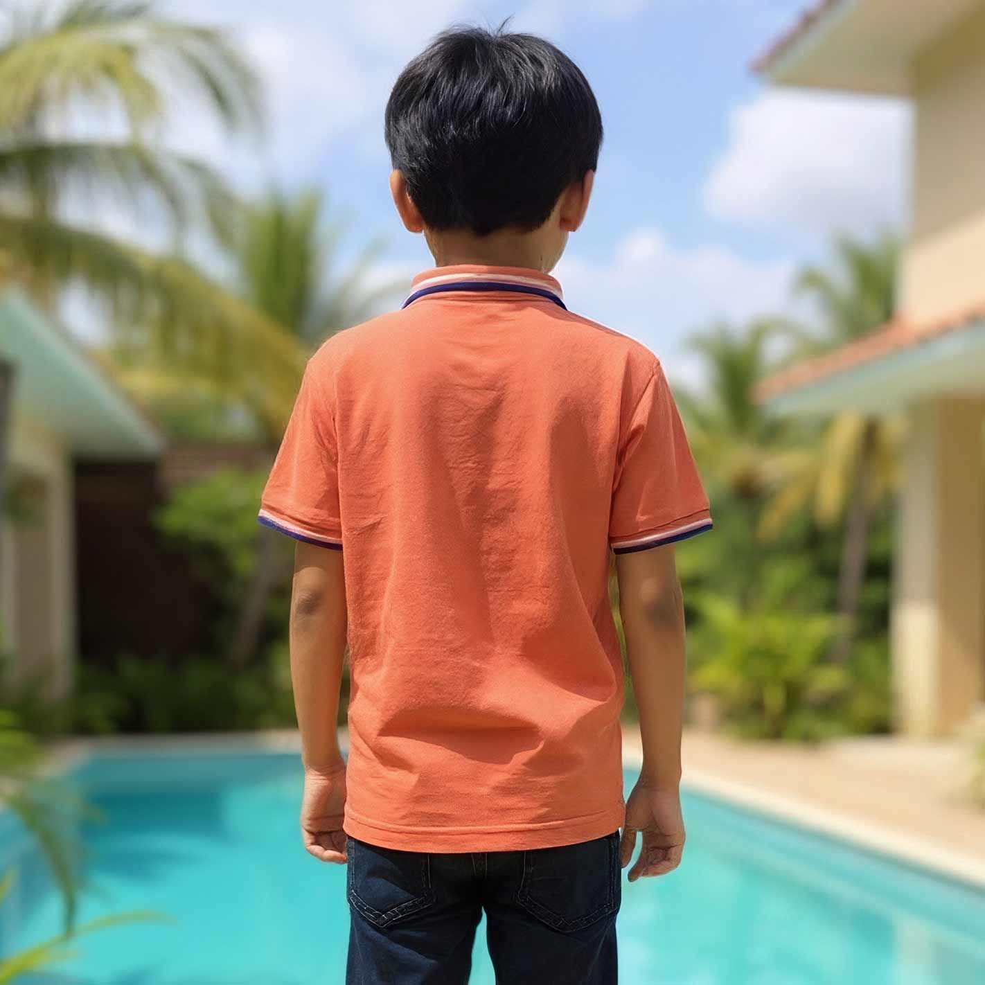 Back view of a Kid wearing an WYO Carrot polo shirt by a pool with greenery and buildings in the background
