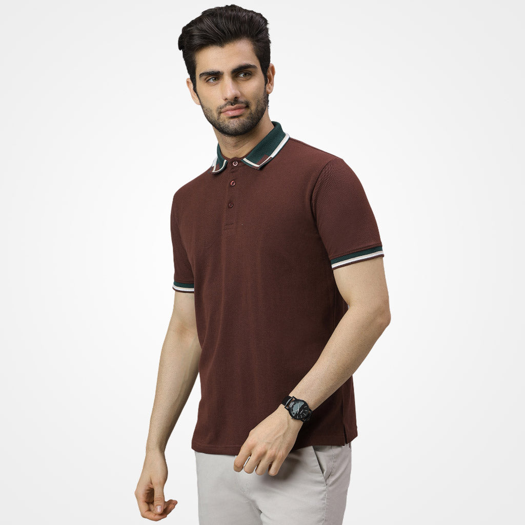 Man wearing a WYO brown polo shirt with white pants on a light gray background